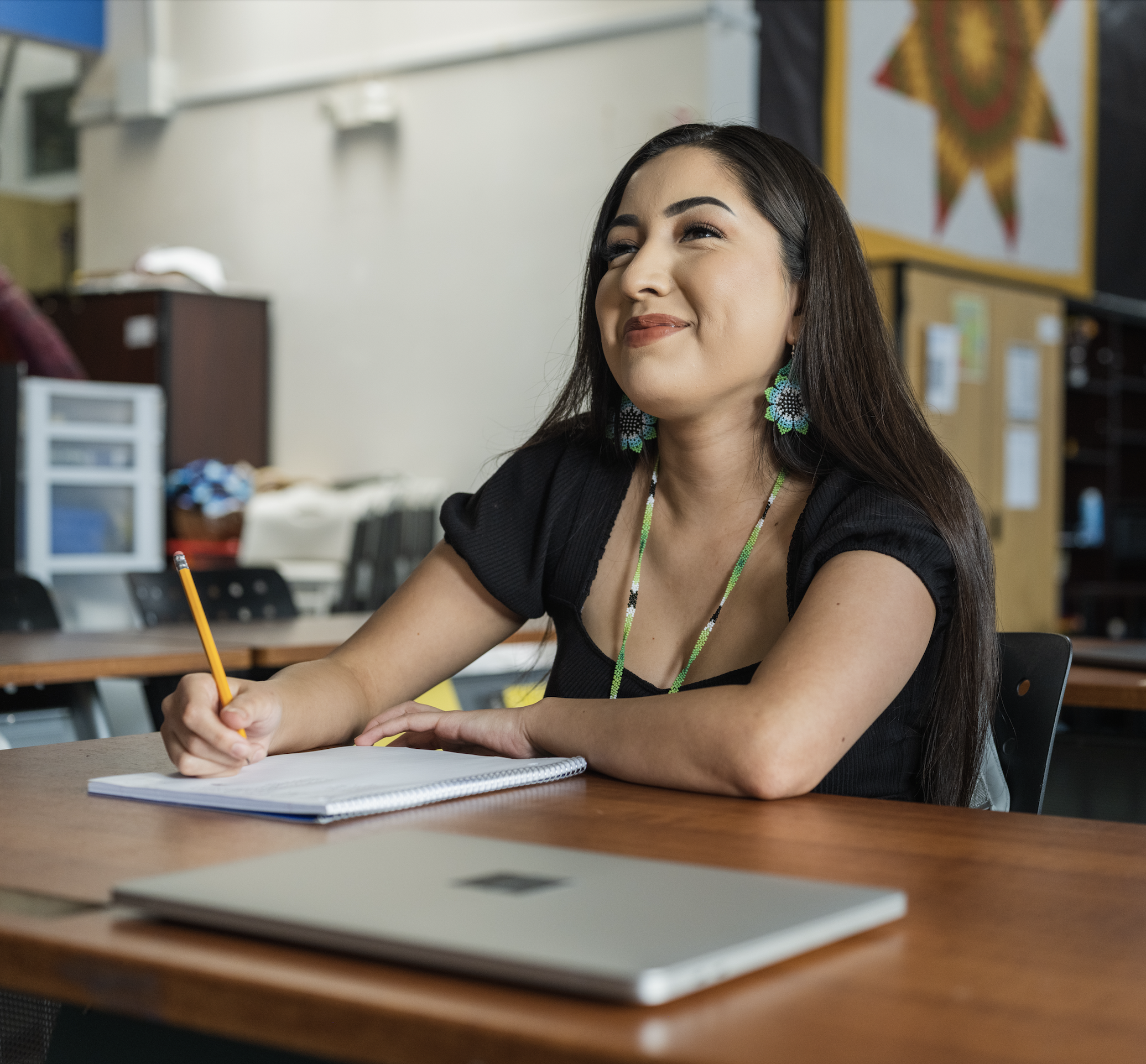 Picture of an Indigenous young woman sitting at a desk and taking notes while smiling