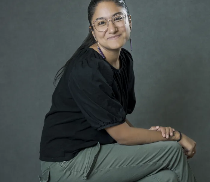 Photo of Nadia sitting on a stool looking at the camera with a soft smile