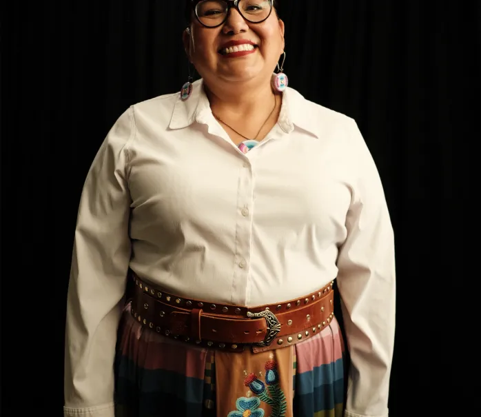 Image of Donna Chrisjohn, wearing a white long sleeve shirt, ribbon skirt, and leather belt